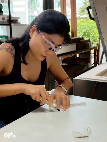 Workshop guest wearing protective goggles shaping a glass dish on a workbench at Art Glass Centre, Singapore