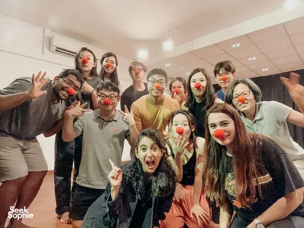 Singapore clowning workshop where a group with clown noses laughs and poses with raised arms during an improvised team game, team building Singapore