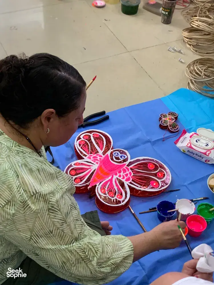 Ho Chi Minh City artisan painting red and pink lantern crafts on a blue tablecloth in a craft workshop, Viet Awesome Tours