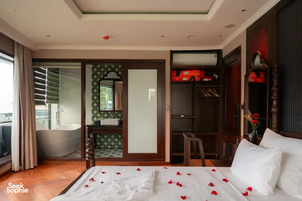 Luxury cruise suite cabin with private bath tub alcove and rose‑petal towel swans on the bed, Cat Ba 2D1N