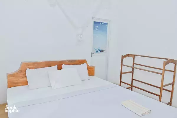 Clean lodge bedroom with a wooden bed, white linens and a simple wall fan, at Splendid Lake View Safari Lodge in Udawalawe