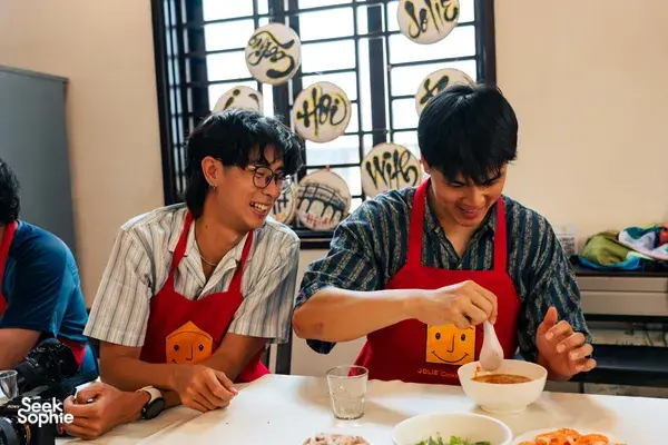 Guests wearing aprons preparing food at a table during Jolie Cooking Class in Hoi An, with bowls and ingredients ready