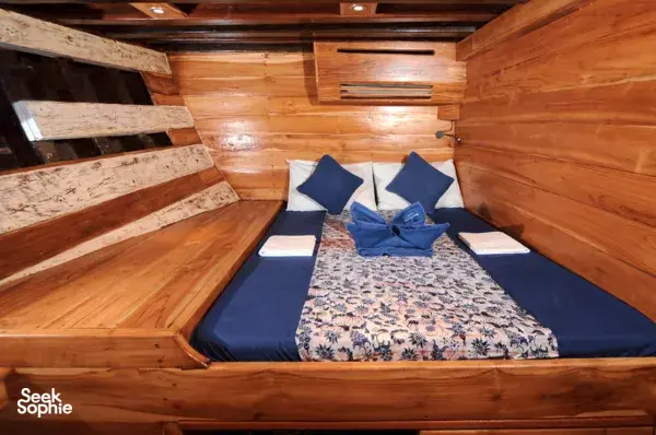 Bed made up with navy towels and patterned bedding inside a wooden Moana Dive cabin on a 6D5N liveaboard for Komodo Island