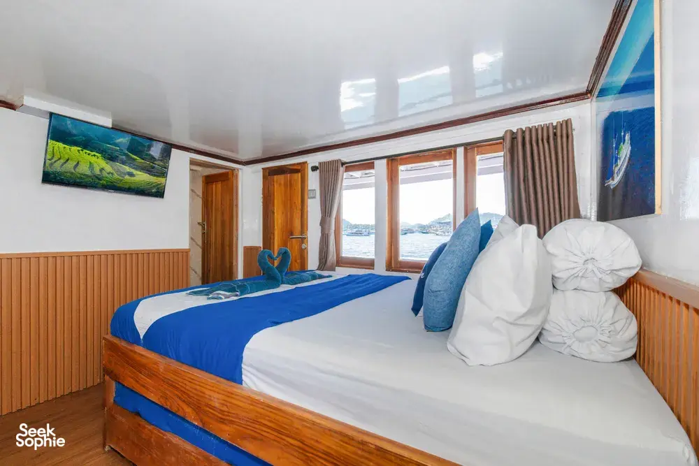 La Famille cabin with towel swans beside blue bedding, large windows with ocean views and wooden panelling, Labuan Bajo