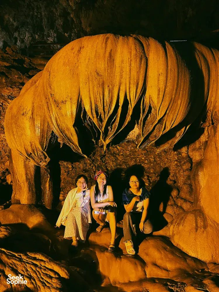 Three travellers posing in a cave under a glowing yellow rock formation during a Cao Bang motorbike journey