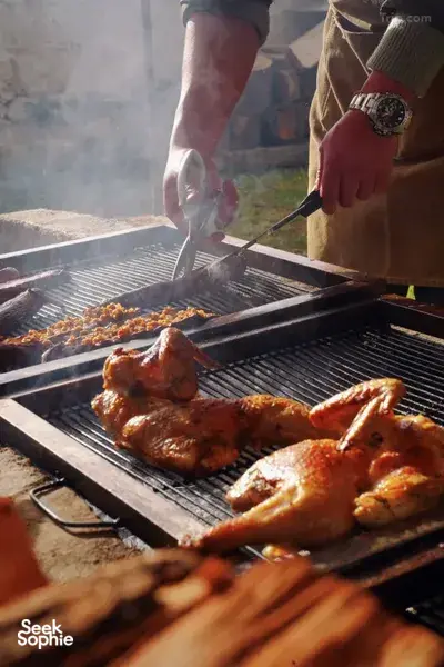 Hands turning skewered chicken on a charcoal grill at an outdoor camp during a Tibetan mountain valley stay in Shangri-La
