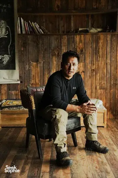Khampa Caravan host seated in a rustic wooden room in Shangri-La, meeting Tibetan cultural guide during a home visit