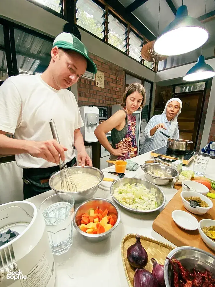 Shared cooking session at Kebun Lidstari farmhouse kitchen in Langkawi, with people chopping vegetables and stirring pots during prep