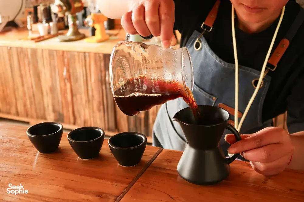 A taster pours dark coffee into a small server for a cupping at the family-run specialty coffee workshop in Lijiang