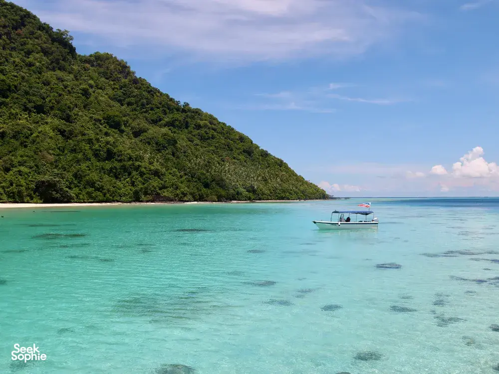Bot yang berlabuh di teluk biru kehijauan di Semporna untuk pengalaman mendaki dan snorkeling Bohey Dulang & pulau-pulau bersama Bigfin Divers