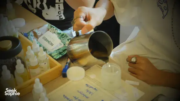 A cup pouring fragrance concentrate into a coco-soy candle jar on a Singapore worktable during a candle workshop