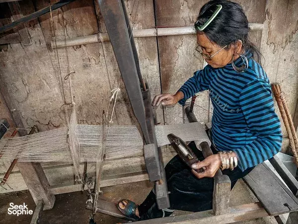 Weaver working a wooden loom with metal tools, patterning fabric panels inside a traditional craft room, Sapa