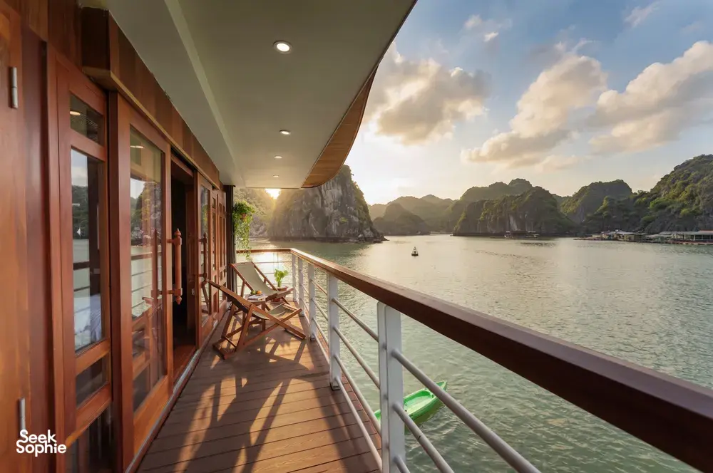Sunlit wooden cruise balcony with lounge chairs and balcony rail, overlooking calm karst waters on a boutique cruise in Cat Ba
