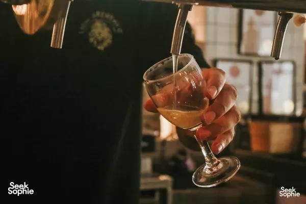 Hand holding an amber beer glass as beer pours from a tap at Lion Brewery Co brewpub in Singapore, warm lighting