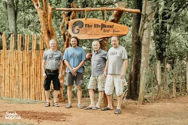 Group standing outdoors in front of the Elephant Next Door welcome sign in Udawalawe, surrounded by trees