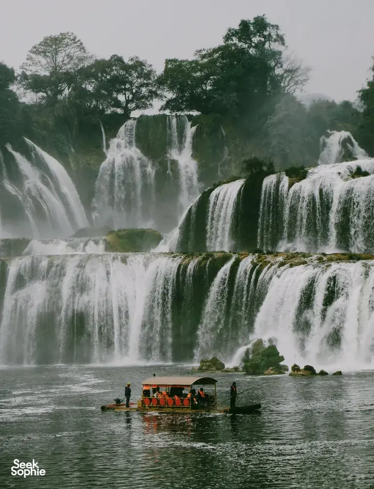 Cascading waterfall in Cao Bang with a small boat floating on the river below, Ha Giang Expeditions motorbike tour