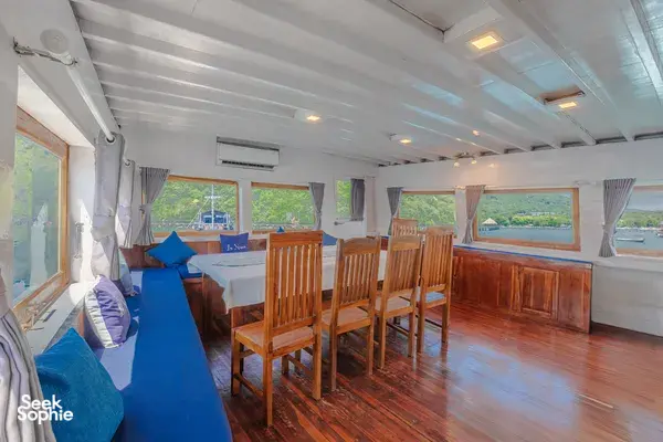 Onboard lounge with blue bench seating, wooden dining chairs and panoramic windows, part of a 3-day join-in Komodo boat trip in Labuan Bajo