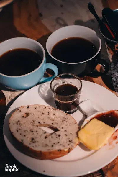Plate of bagel with butter and cups of dark coffee at a hands-on coffee roasting and brunch experience, workshops in Singapore