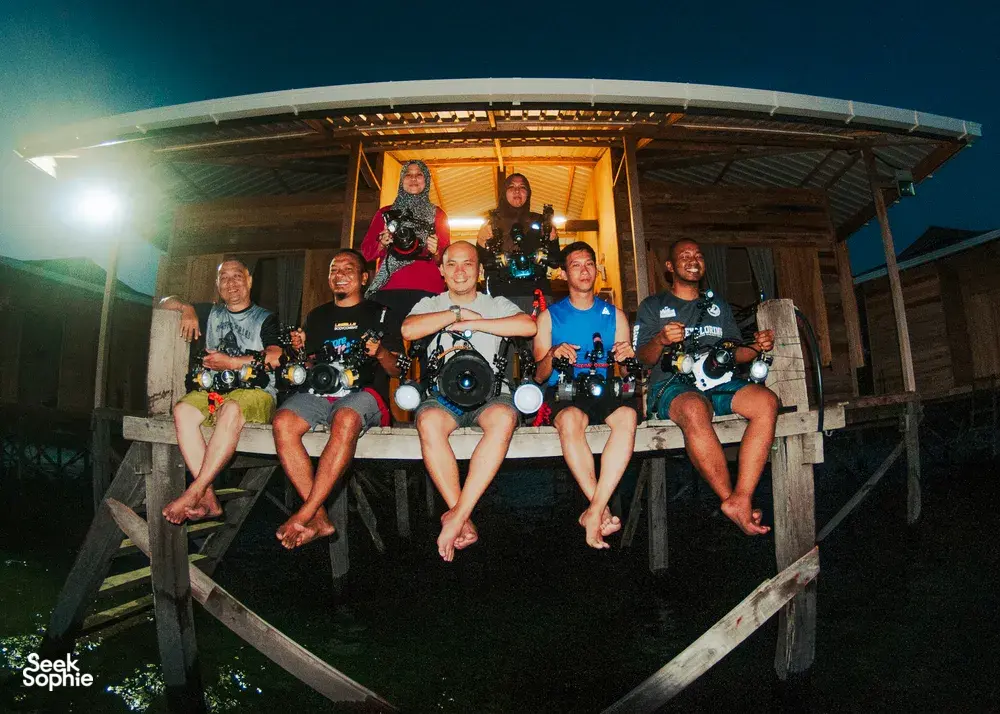 Scuba divers posing on a boat at night with tanks and cameras, led from Luma Selakan in Semporna for macro dives