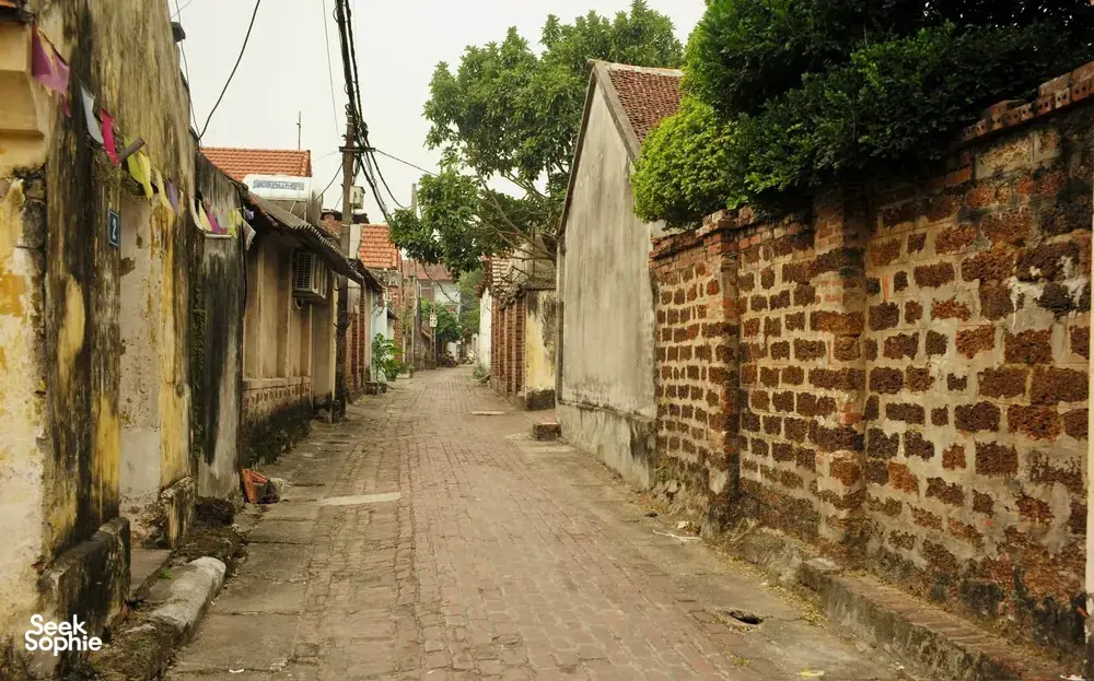 Cobblestone lane through Duong Lam ancient village near Hanoi, with brick walls and tiled rooftops stretching into the distance