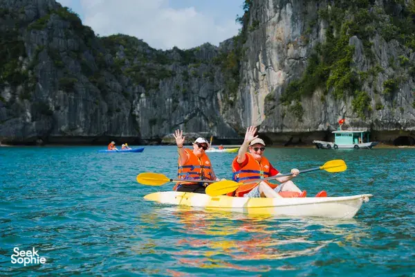 Kayakers in orange life jackets paddle through calm waters near limestone karsts on a Cat Ba cruise