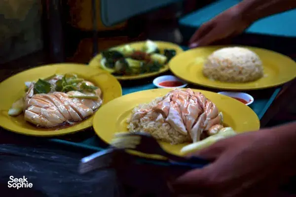 Hands carrying yellow plates of hawker food at a Singapore stall, showcasing Singapore hidden gems from the city’s hawker culture