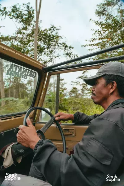 Ayla Tour guide driving an open jeep along a green winding road during the Mount Merapi jeep adventure in Yogyakarta