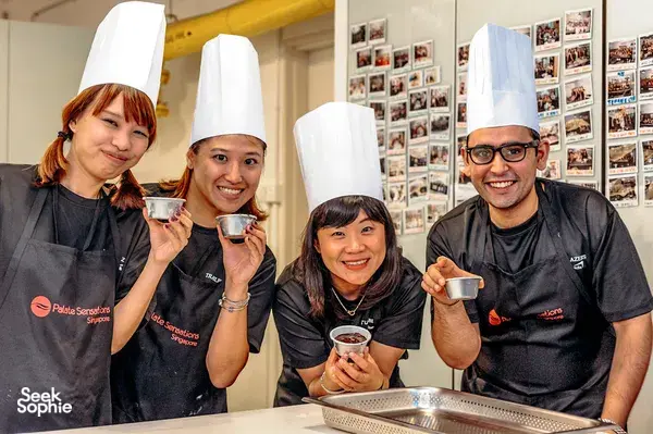 Smiling team in chef hats toasting paper cups at Palate Sensations SGâs baking experience in Singapore