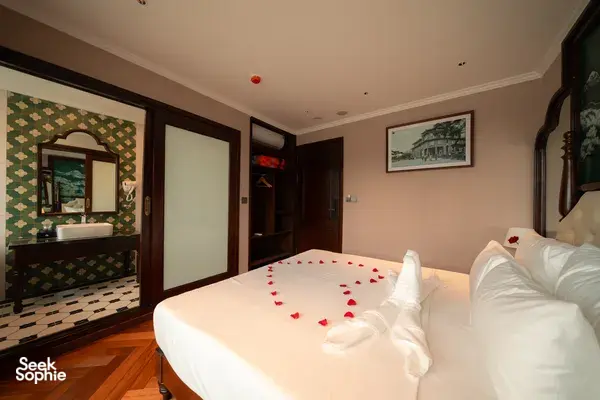 Cruise cabin bedroom with mirror and bathroom doorway, king bed with rose‑petal towel swans, Cat Ba 2D1N