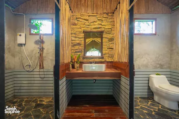 Rustic camp bathroom in Thailand with a stone shower wall, tiled floor, basin vanity and a white toilet in view