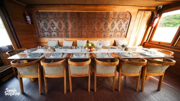 Banquet-style dining set with woven-back chairs on a phinisi cruise, ready for shared meals in Labuan Bajo