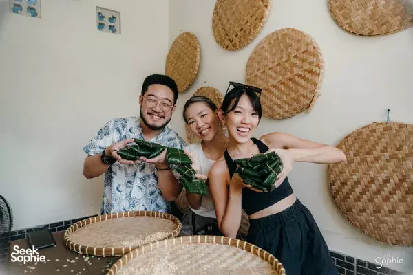 Tempe-making in Bali: three friends smiling while presenting green banana-leaf parcels of tempe to the camera