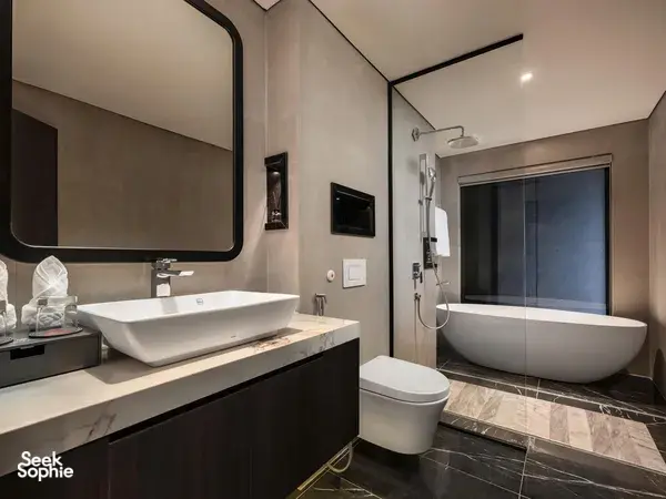 En-suite bathroom aboard Tulip Cruise with oval mirrors, vanity sink, toilet and bathtub, glass view of karst on Halong Bay