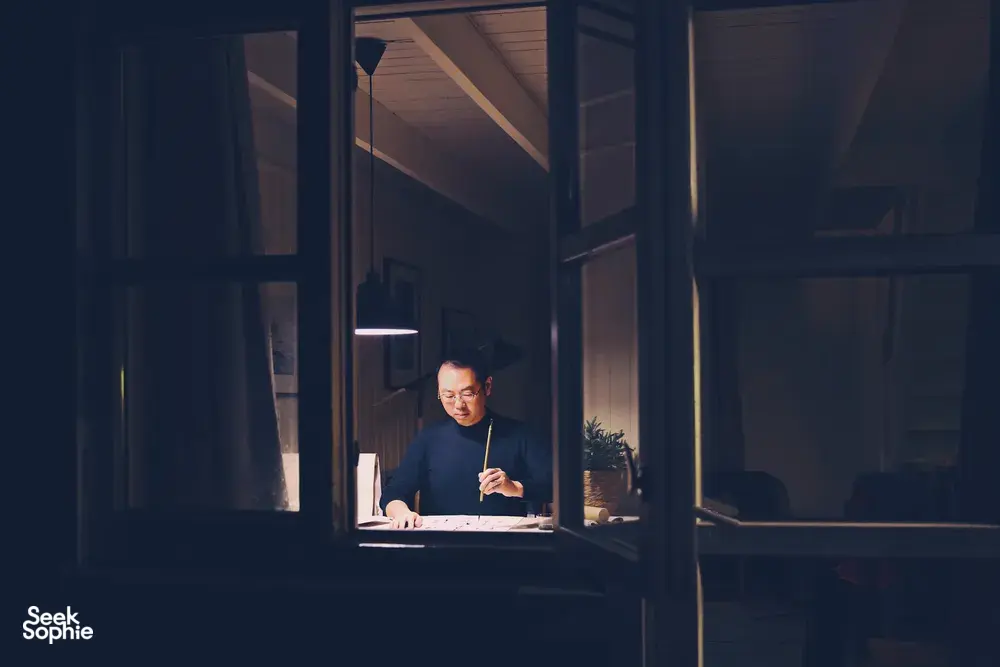 Chong Zheng Calligraphy instructor writing Chinese brush strokes by a window in Singapore, preparing a blessing at workshops in Singapore