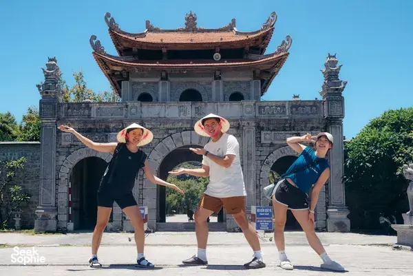 Three travellers posing with arms out in front of an ornate stone gate in Ninh Binh on a private day tour