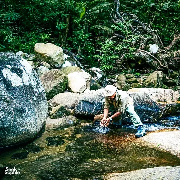 Herbalist-guided gentle forest walk at Gunung Raya, Langkawi with Darulaman Sanctuary: crossing a stream over boulders