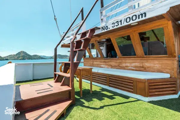 Sleek phinisi deck with artificial grass, wooden steps and seating, with mountains and sea in the distance on a Komodo cruise, Labuan Bajo