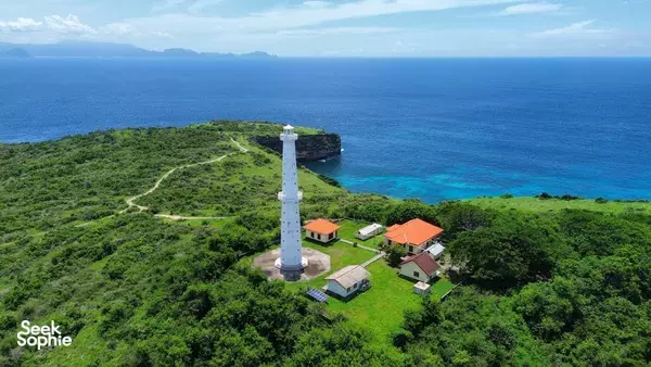 Aerial view over Lombok’s coast: a green headland with a white lighthouse and small buildings, surrounded by blue ocean