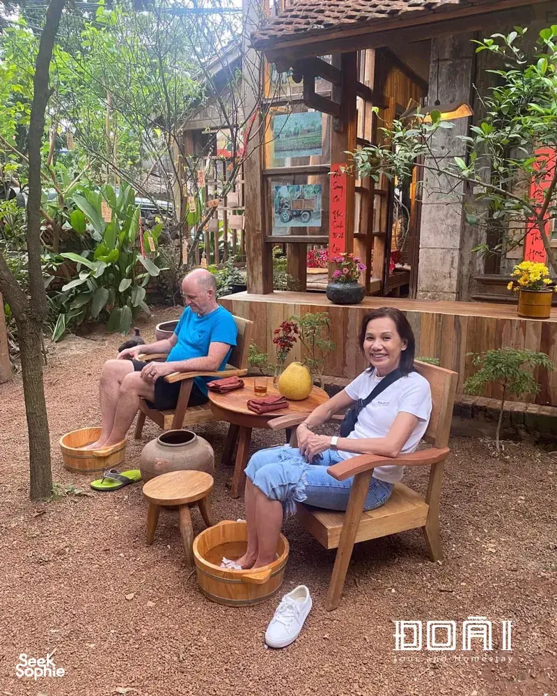 Guests seated at a wooden table during a craft tea moment in an ancient village near Hanoi, surrounded by potted plants