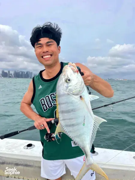Smiling angler holding a large silver catch on the boat deck with Singapore skyline over choppy sea during a Southern Islands fishing trip