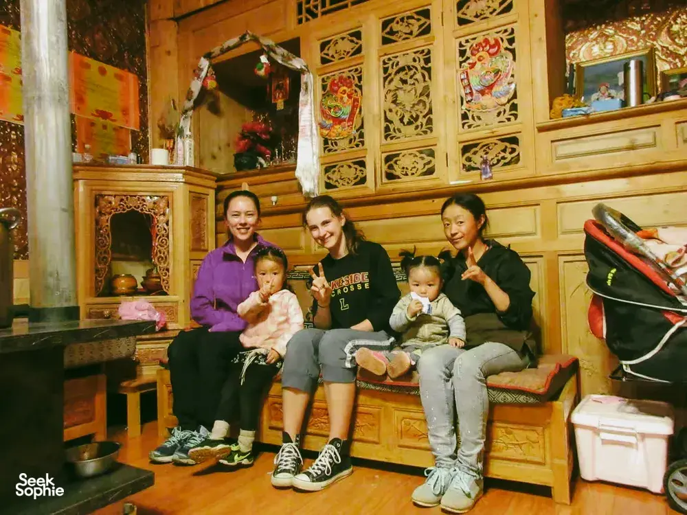 Family gathering indoors in a Tibetan homestay in Shangri-La, with two adults and two children smiling on a bench