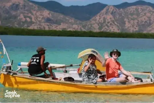 People seated on a yellow boat over clear turquoise water with hills in the distance, on a Komodo day trip from Labuan Bajo