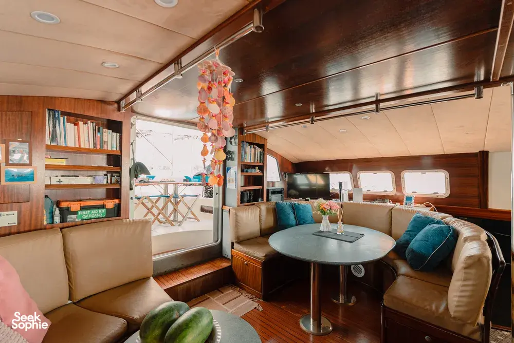 Mawali catamaran lounge in Kota Kinabalu, Sabah, with cushioned seating, a dining table and books for relaxing between stops