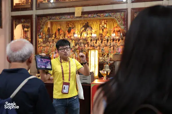 Hey Lad Tour guide gesturing in front of an illuminated Chinese shrine while leading Hidden Chinese Rituals at night in Singapore, Singapore hidden gems