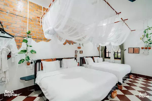 Canopy bed in a bright Mekong Delta homestay room, set with crisp white linens and mosquito net beside two doors and decor
