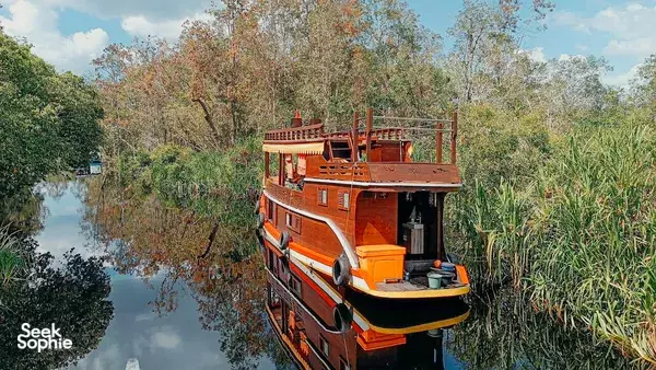 Orange klotok cruise boat gliding on a calm river through the Tanjung Puting rainforest near Pangkalan Bun, Borneo