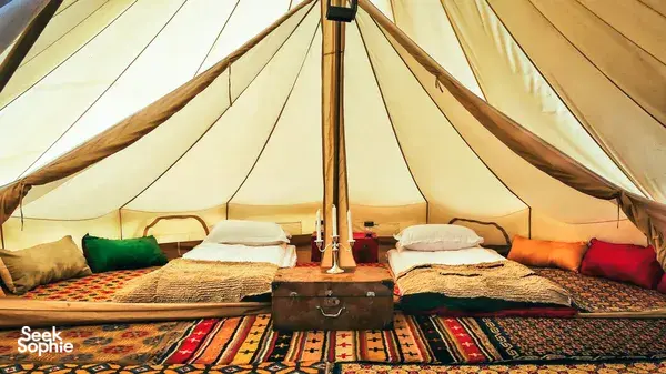Cozy camp bed inside a canvas tent in Shangri-La’s remote valleys, neatly made with pillows, rugs and a bedside lantern