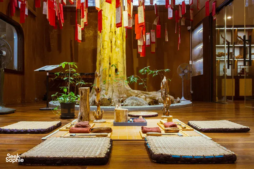 Agarwood exhibition room in Hanoi with carved wood specimens on floor mats beneath hung Vietnamese banners