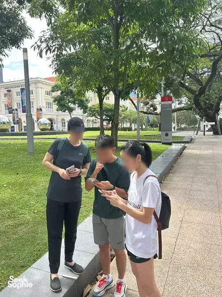 Participants on the Survive The Collapse sustainability scavenger hunt in Singapore, reading challenge cards on a shaded park path