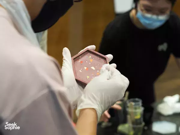 Gloved hands display a pale pink hexagonal terrazzo coaster with flecks at marble & terrazzo coaster making workshops in Singapore
